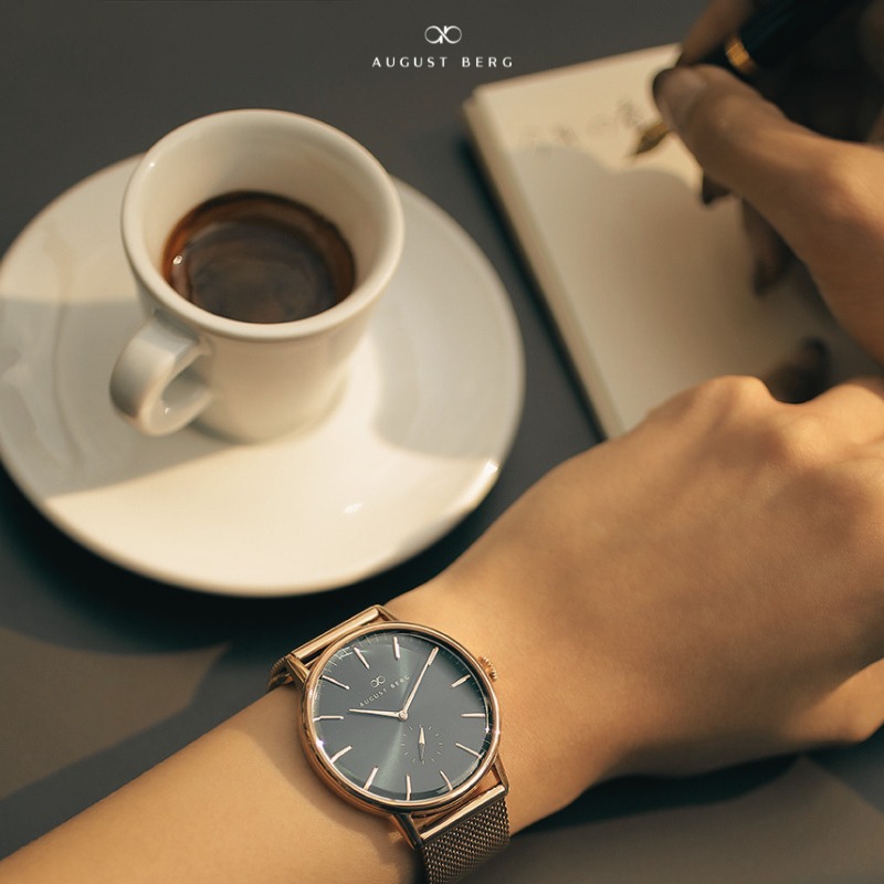 August Berg rose gold watch on a wrist beside a coffee cup