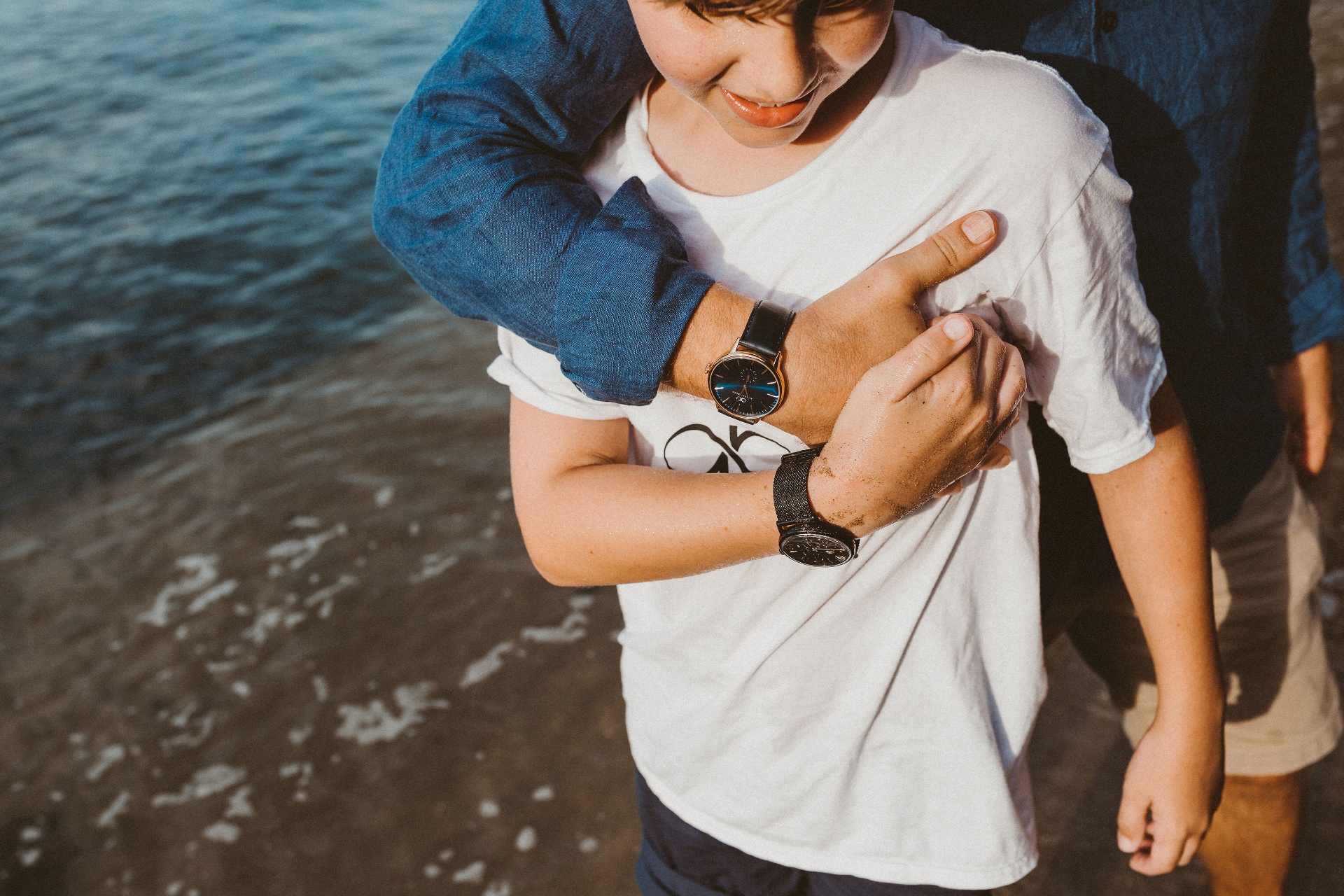 Father embracing his son on the shoreline, both wearing August Berg watches