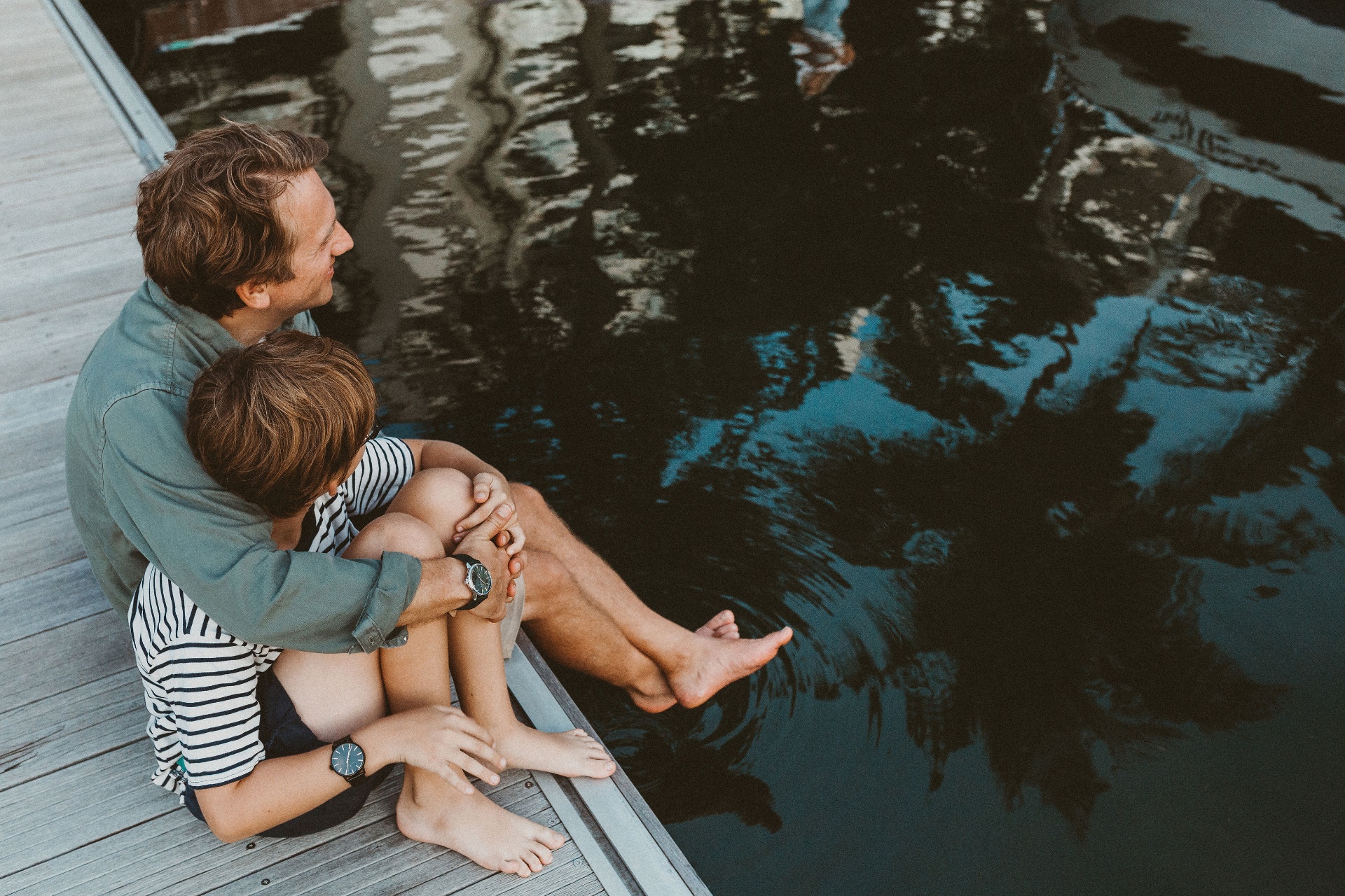 Father and son sitting at the water's edge, sharing a quiet moment